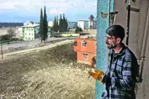 Ο Αχμέτ Αλτινόζ στέκεται προβληματισμένος πίσω από το παράθυρο στο σπίτι των γονιών του, οι οποίοι μόλις πήραν το μήνυμα από την κυβέρνηση που τους ειδοποιεί πως θα πρέπει να μεταφερθούν σε άλλη περιοχή, νοτιότερα στο Χατάι.